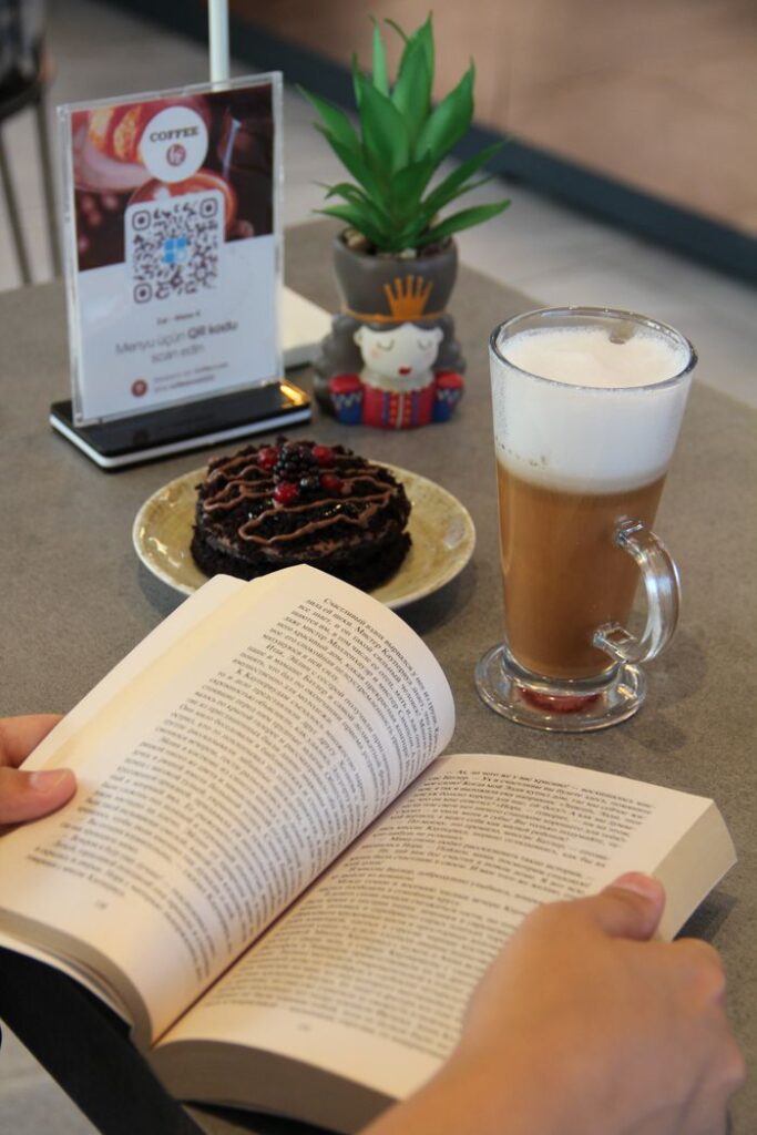 Relaxed reading setup with a book, coffee, and dessert on a cafe table.